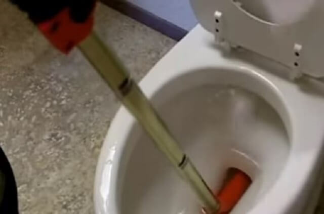 A toilet auger being used to clear a clogged toilet